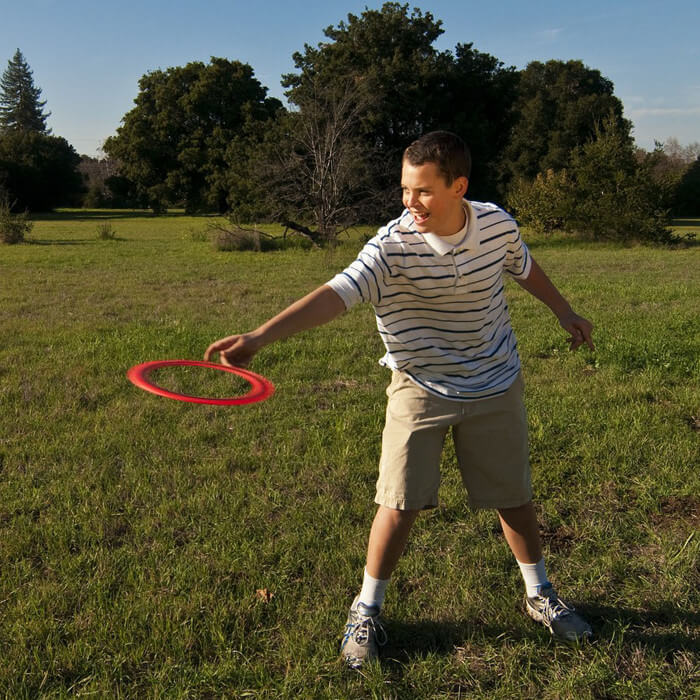 Aerobie - Junge wirft orangen Ring auf Wiese Aerobie - Junge wirft orangen Ring auf Wiese